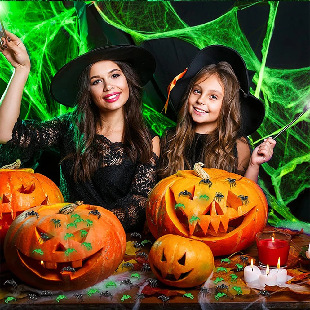 Glow-in-the-Dark Spider Web – two people in witch hats behind jack-o'-lanterns draped in glowing web